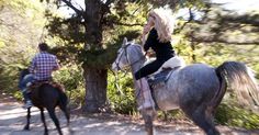 a woman riding on the back of a gray horse next to a man in plaid shirt