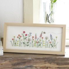 a cross stitch pattern with flowers in it on a wooden table next to a window