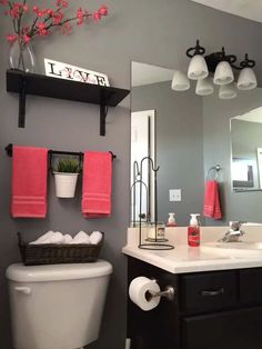 a white toilet sitting under a bathroom mirror next to a black vanity and shelf with pink towels on it