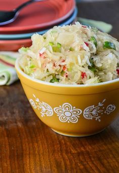 a yellow bowl filled with coleslaw sitting on top of a wooden table next to plates