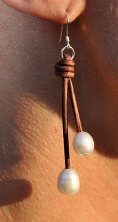 the back of a woman's ear with two white pearls hanging from leather cord