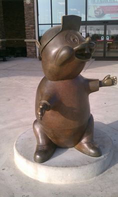 a statue of a pig sitting on top of a cement slab in front of a building