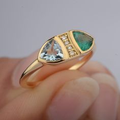 a close up of a person holding a gold ring with an oval cut diamond and pear shaped green tourmaline