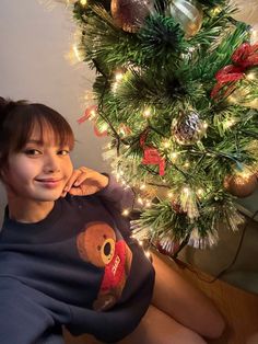 a woman sitting in front of a christmas tree wearing a t - shirt with a teddy bear on it