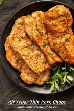 some fried food on a black plate with green garnish and seasoning sprigs