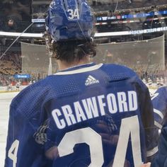 a hockey player in blue jersey standing next to an ice rink