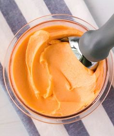 a spoon in a glass bowl filled with orange colored food and sitting on a striped table cloth