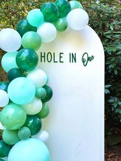 a white grave with green and white balloons on it that says hole in one, surrounded by greenery