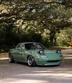 a green sports car parked on the side of a road in front of some trees