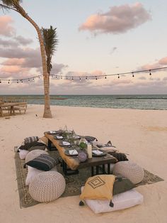 a picnic table set up on the beach with pillows and place settings laid out in front of it