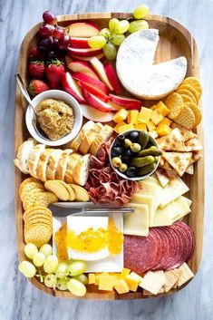 a wooden platter filled with different types of cheeses and crackers, fruit