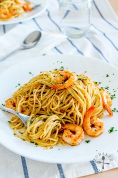 pasta with shrimp and parsley on white plate next to glass of water, fork and spoon