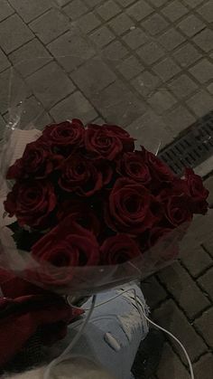 a bouquet of red roses sitting on the ground next to a person's feet