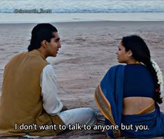 a man and woman sitting on the ground talking to each other with an ocean in the background