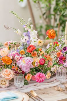 an arrangement of colorful flowers in vases on a table with silverware and place settings