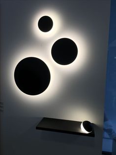 three circular lights mounted on the wall above a shelf in a room with white walls