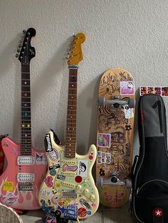 three guitars are lined up next to each other with stickers all over them on the wall