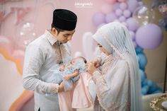 a man and woman holding a baby in front of a cake with balloons on it