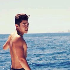 a young man standing on top of a sandy beach next to the ocean with his shirt off