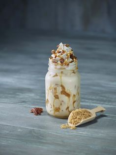 a jar filled with whipped cream and nuts next to a spoon on a wooden table