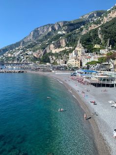 the beach is crowded with people and umbrellas in the water, along with mountains