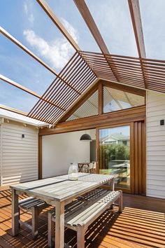 a wooden deck with a table and bench under a pergolated roof overhang