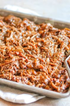 a casserole dish with shredded meat in it on a white tablecloth next to a spoon