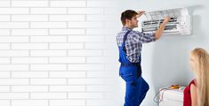 a man in overalls standing next to a woman with an air conditioner on the wall