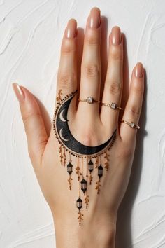 a woman's hand with tattoos on it and a crescent shaped necklace hanging from the wrist