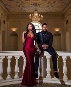 a man and woman in formal wear posing for a photo on a balcony with chandelier