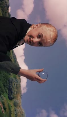 a young boy holding a glass ball in his hand while standing next to a cliff