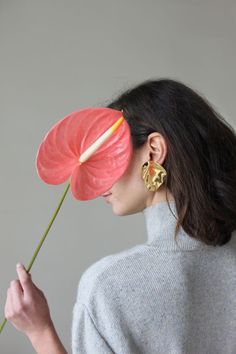 a woman holding a flower in front of her face and wearing earrings to the side