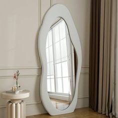 a large white mirror sitting on top of a wooden floor next to a small table