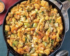 a skillet filled with cauliflower and shrimp next to a bowl of seasoning