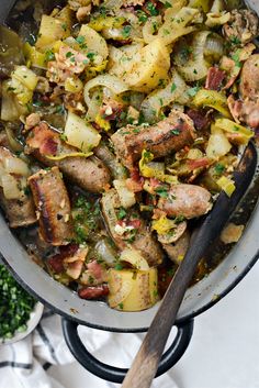 a pan filled with meat and vegetables on top of a table next to a wooden spoon