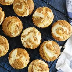 twelve cupcakes with white frosting on a cooling rack next to a napkin