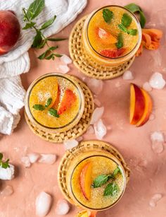 three glasses filled with fruit and ice on top of a pink surface next to peaches