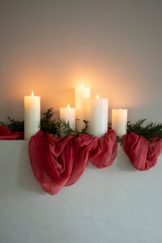 candles are lined up on a mantle with red scarfs and evergreen branches around them