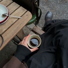 a person sitting at a table with a cup of coffee in their hand and a plate on the table