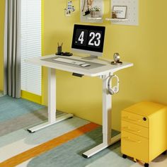 a computer desk with a clock on it in front of a yellow wall and colorful carpet