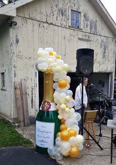 a champagne bottle with balloons attached to it in front of a building and a speaker