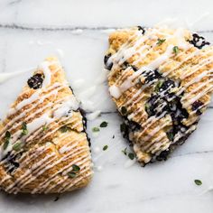 three scones with blueberries and cream drizzled over them on a marble surface