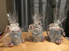 three mugs with candy canes wrapped in cellophane and sitting on a table