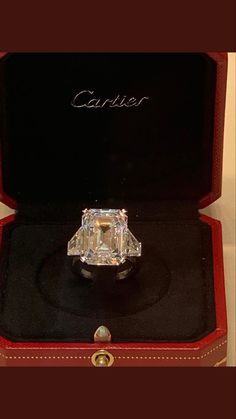 a fancy diamond ring sitting in a red case on top of a black box with the word cartier written above it