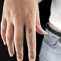 a person's hand with a small tattoo on the middle finger and an upside down ring