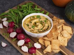 a bowl of hummus dip surrounded by chips and radishes on a cutting board