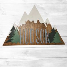 a wooden sign that says hudson with mountains in the background on a white wood wall