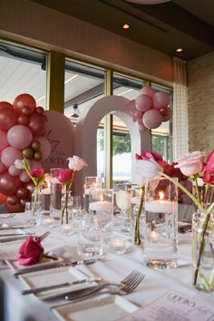 the table is set for a party with pink and white flowers, candles, and heart shaped balloons