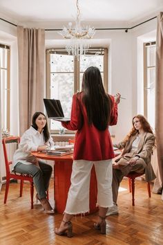 two women sitting at a table in front of a window and one woman standing up