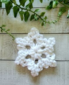 a crocheted snowflake sitting on top of a wooden table next to a plant